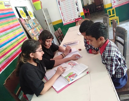 MIS students tutoring young children in a village classroom, engaging in peer teaching and literacy support.